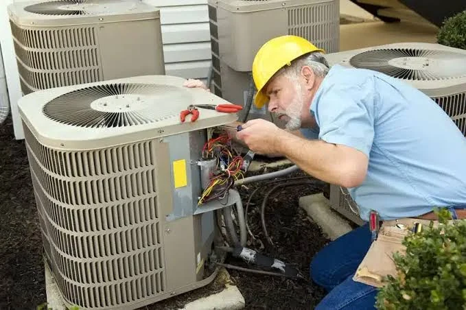 Technician inspecting electrical components in an outdoor HVAC system