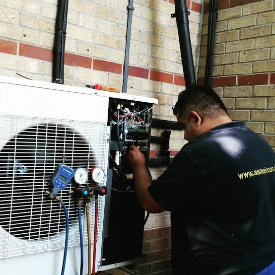Technician inspecting an open air conditioning service panel beside a brick wall